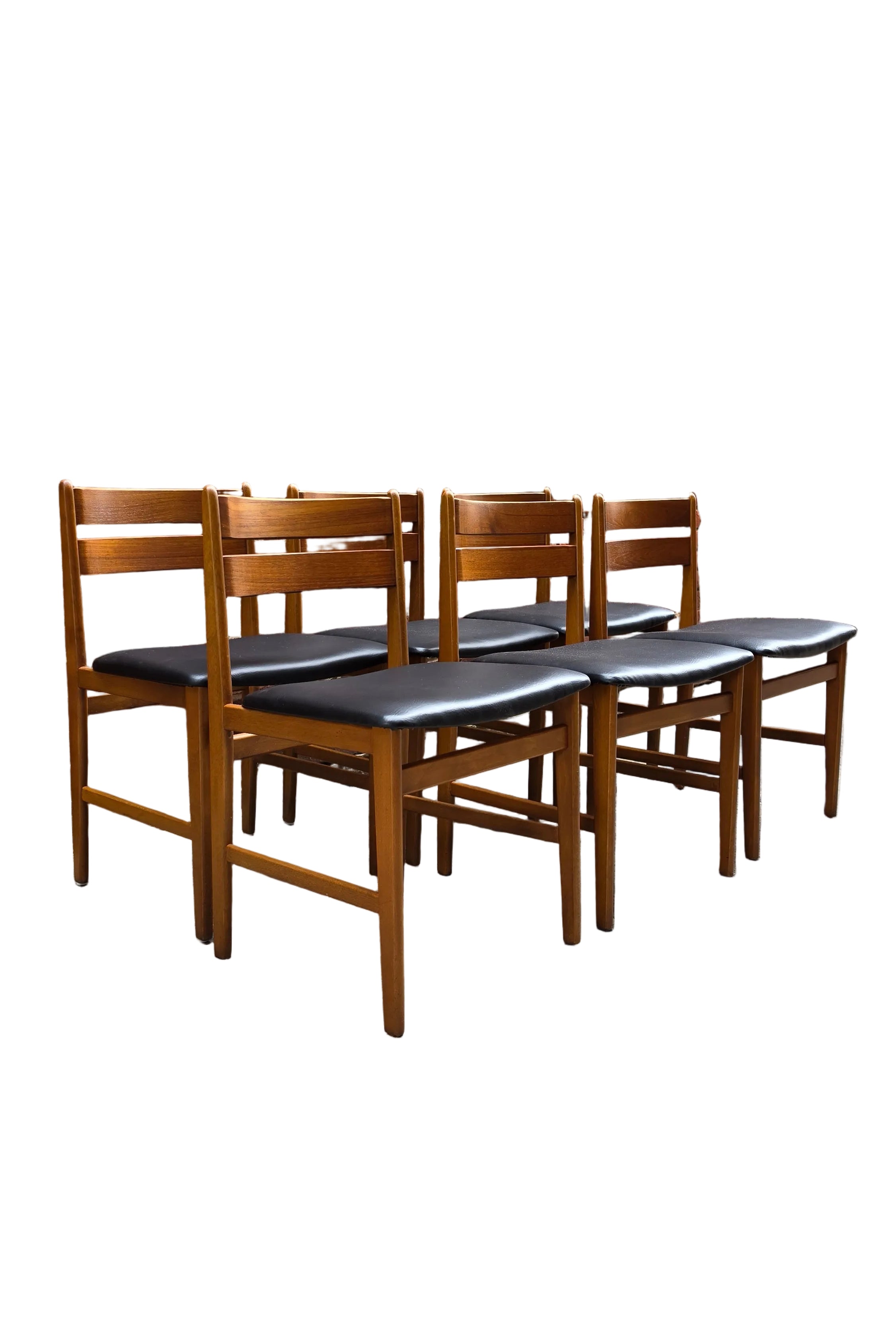 Six teak wooden dining chairs with black upholstered seats arranged in a row against a red brick wall on a concrete floor.